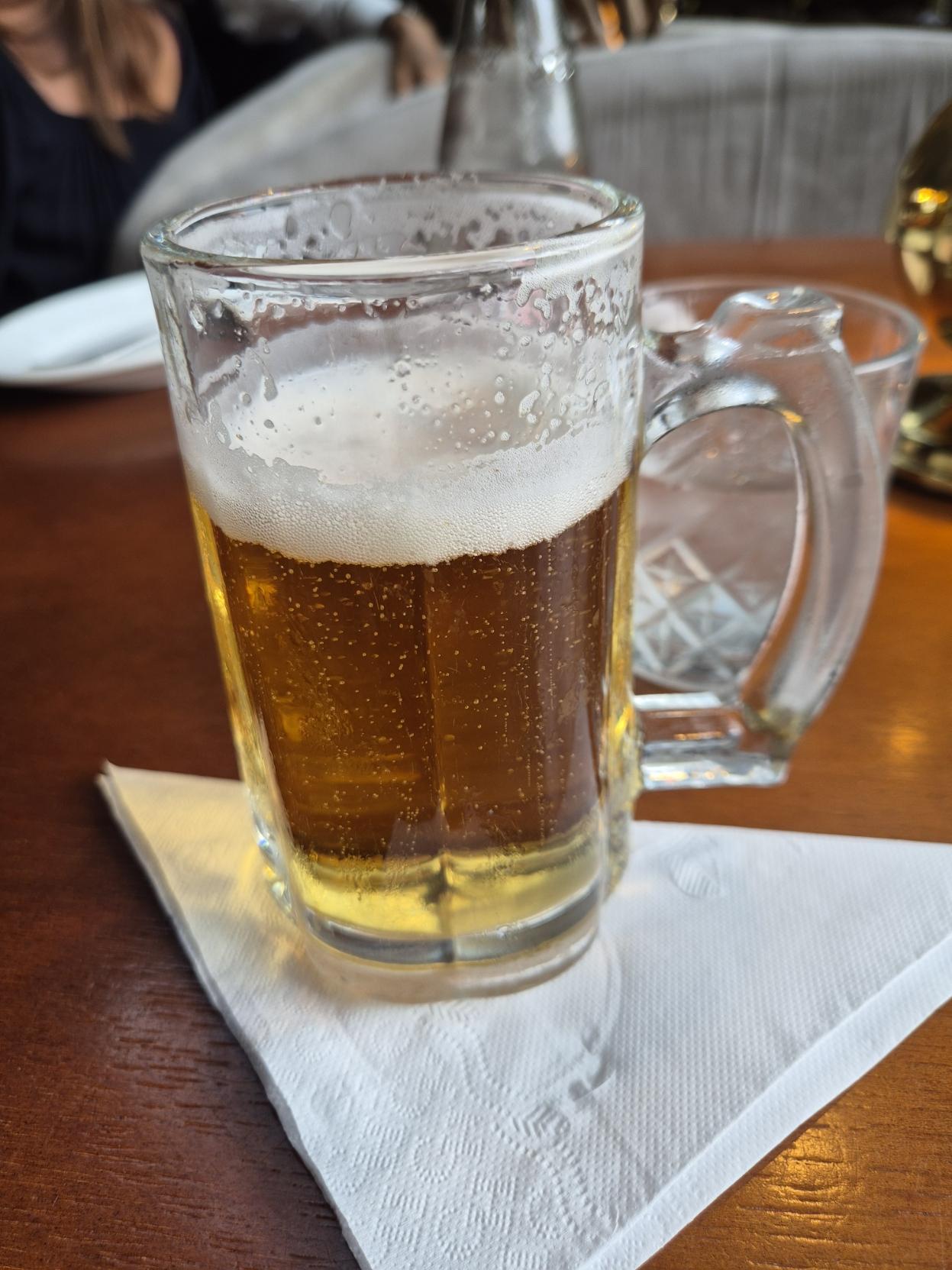 Foto de chopp em cima de uma mesa de madeira com um copo de água com gás logo atrás